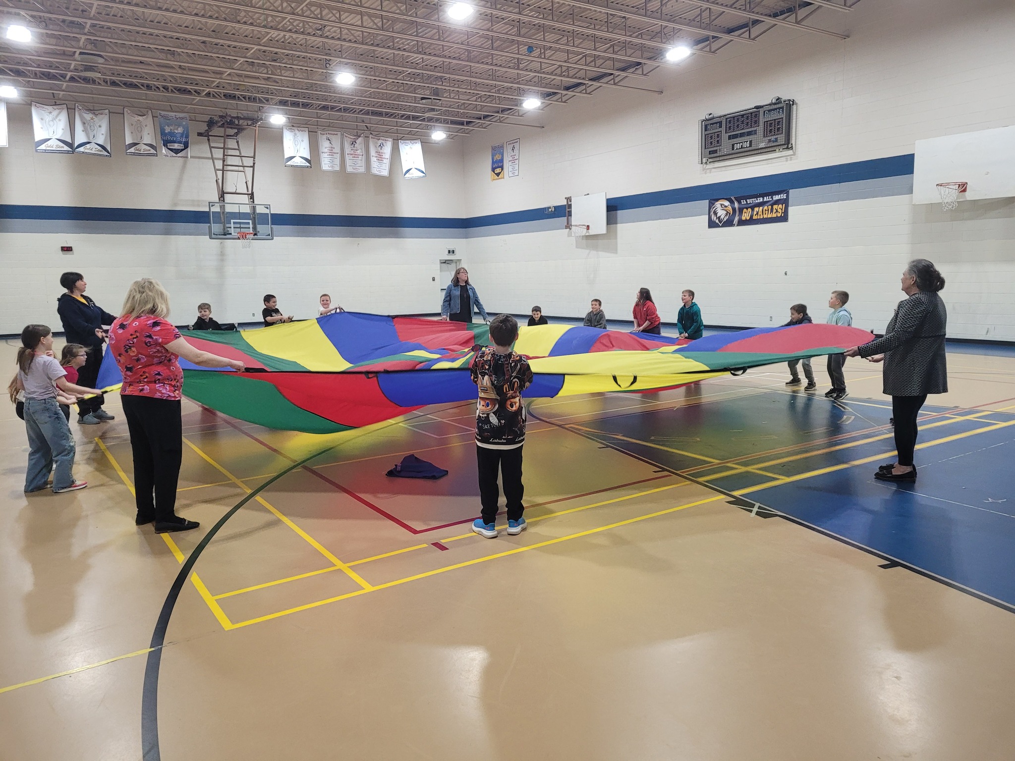 Children and community members using a colourful parachute in a school gym